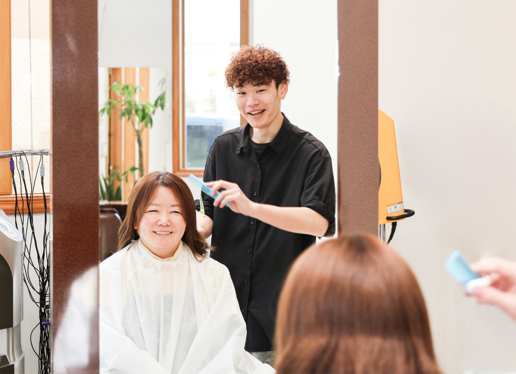 笑顔でお客さんのカットをするスタイリスト